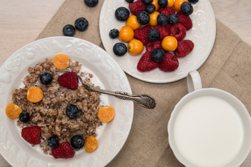 Buckwheat breakfast with berries on white plate, blueberry, golden berry, physalis, raspberry, milk