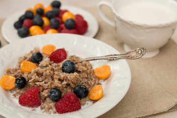 Buckwheat breakfast with berries on white plate, blueberry, golden berry, physalis, raspberry, milk
