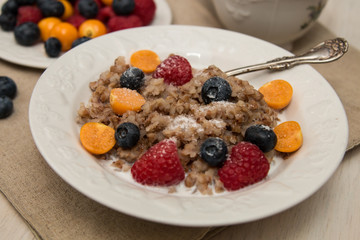 Buckwheat breakfast meal with berries on white plate, milk, blueberry, golden berry, physalis, raspberry 