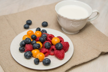 Buckwheat breakfast meal with berries on white plate, milk, blueberry, golden berry, physalis, raspberry 