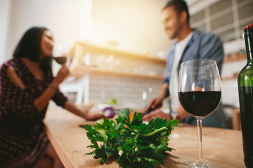 Glass of red wine on kitchen counter with couple in background