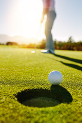 Golfball am Rand des Lochs mit Spieler im Hintergrund