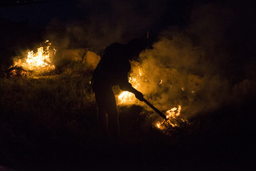 Hell fire - man silhouette spreading a weeds fire on the beach to clear his yard under the night.