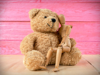 Wooden puppet with a teddy bear and a pink wooden background.