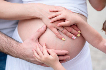The hands of a father and daughter on the belly of a pregnant mother.