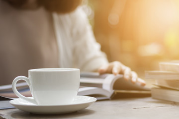 Woman is reading a book and drinking coffee in the garden.