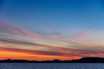 colorful sunset at Balaton lake in summer - thin clouds, dark water and mountains in background