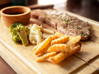 Delicious steaks with seasonings and herbs on wooden dish.
