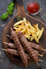 Above view of grilled balkan cevapcici or skinless beef sausages on skewers with roasted potato, vertical shot