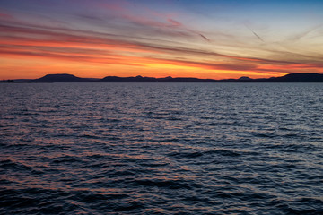 colorful sunset at Balaton lake in summer - thin clouds, dark water and mountains in background