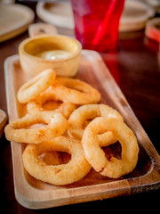 Fried breaded onion rings with sauce on a classic wooden plate.