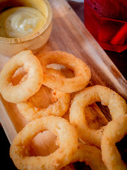 Fried breaded onion rings with sauce on a classic wooden plate.