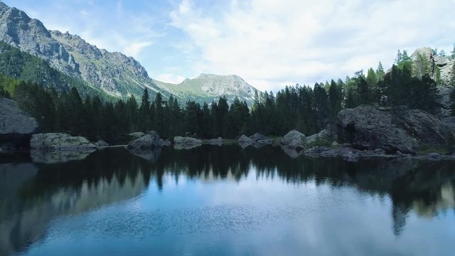 moving backward away from clear blue lake and pine woods forest mountain valley in summer.Europe Alps outdoor green nature scape mountains wild aerial establisher.4k drone flight establishing shot