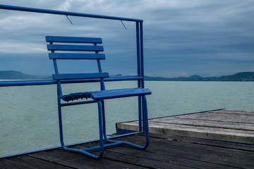blue metal chair on wooden pier at Balaton lake - lonely day, windy and cloudy weather in the summer season