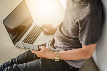 Laptop and smartphone mockup. Closeup of man holding smartphone in hand and laptop on floor.