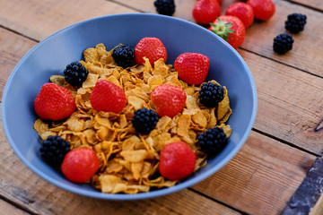 Corn flakes on a strawberry and blackberry on a plate.