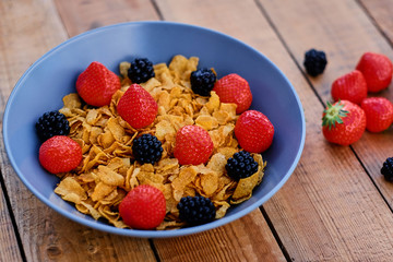 Corn flakes on a strawberry and blackberry on a plate.