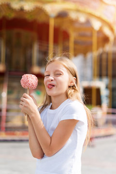Cute Little Girl Eating Candy Apple And Posing At Fair In Amusement Park.