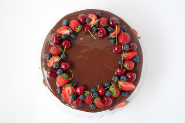 Birthday cake in chocolate with strawberries, blueberries and cherry on white background. Top view....