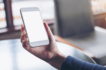 Mockup image of hand holding white mobile phone with blank screen on table in cafe