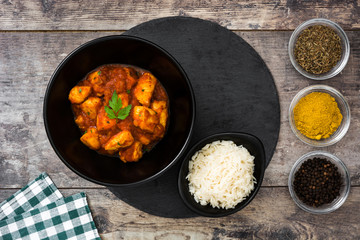 Chicken tikka masala with basmati rice in black bowl on wooden table
