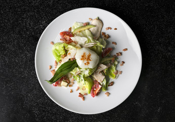 Mix salad with egg poached and chicken on a white plate