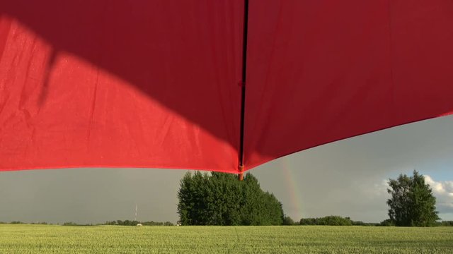 Evening rainbow over farmland fields and red umbrella motion