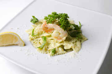 Farfalle with shrimps and pesto sauce on a white plate