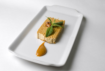 Honey puff cake on a white plate with mint and caramel sauce