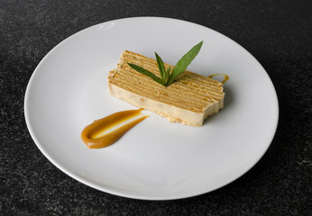 Honey puff cake on a white plate with mint and caramel sauce