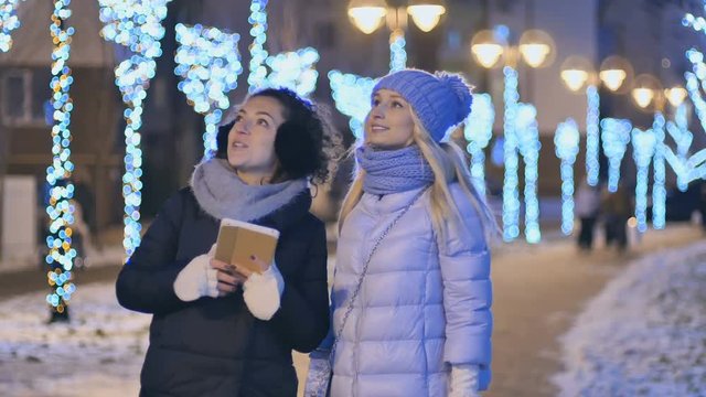 Two young girlfriends looks with surprise at winter evening city