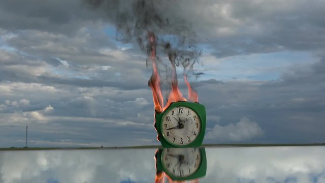 Time and fire concept. Burning  old retro green alarm clock on mirror in space