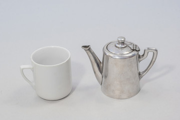 silver teapot and a white tea cup on a gray background