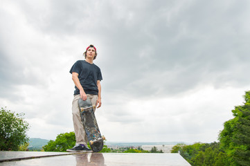 A young skater stands with a skateboard on the background of the landscape of the city