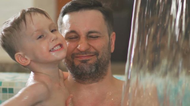 Little boy is entertained in the pool with his father. Father and son have fun in the pool with a waterfall. Waterfall in the pool: the boy and father are playing in the water. Family in the SPA