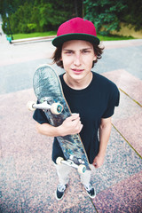A young skater stands with a skateboard on the background of the landscape of the city