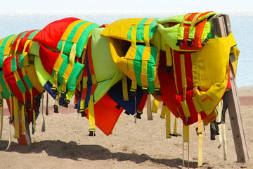 close up of Colorful life jackets with sea and sand background . equipment for safety in water transportation.