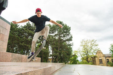 Long-haired skater-teenager in a T-shirt and a sneaker hat jumps an alley against a stormy sky