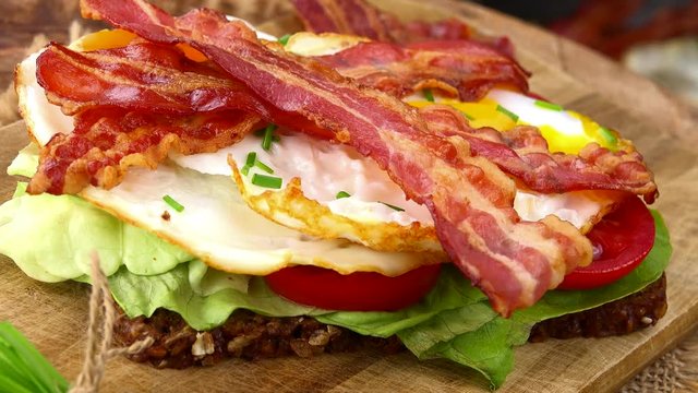 Bacon with fried Eggs rotating on a wooden plate (not loopable; 4K)