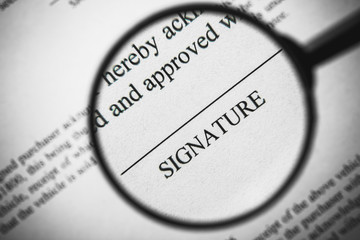 Magnifying glass enlarging signature word on business document.