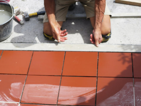 Miglioramento domestico, ristrutturazione - il lavoratore dell'edilizia è piastrellato, adesivo a pavimento in piastrelle di ceramica