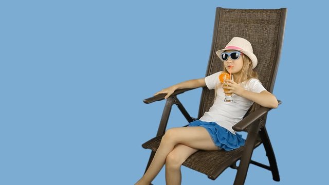Young caucasian girl sitting on chair and drinking orange juice cocktail through straw.