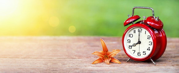 Summer time concept - website banner of a red alarm clock and orange lily flower