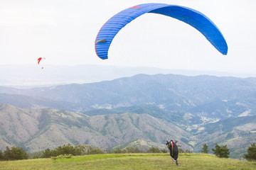 Paraglider on a mountain top preparing to take flight. Flying over a mountain valley in summer sunny day.