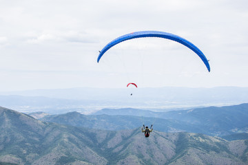 Paragliding in the sky. Paragliders fly over a mountain valley in summer sunny day.