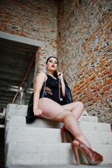 Fototapeta na wymiar Brunette plus size sexy woman, wear at black one piece and leather jacket,with chain at abadoned place sitting on stairs. BDSM theme.