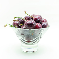 Glass vase with fresh wet cherries on white background