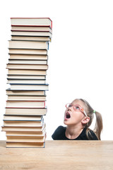 Little girl with glasses looks surprised at a high stack of books, standing on a table, isolated on a white background
