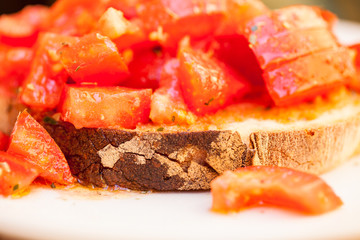 Tasty savory tomato Italian appetizers, or bruschetta, on slices of toasted baguette garnished with basil, close up on a wooden board