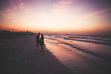 Romantic couple silhouette by ocean at sunset.  Romantic couple walks towards sunset holding hands